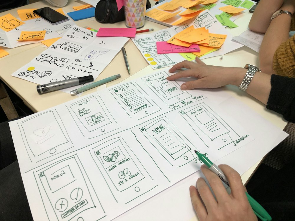 Hand-drawn app wireframes spread across a table during a design review